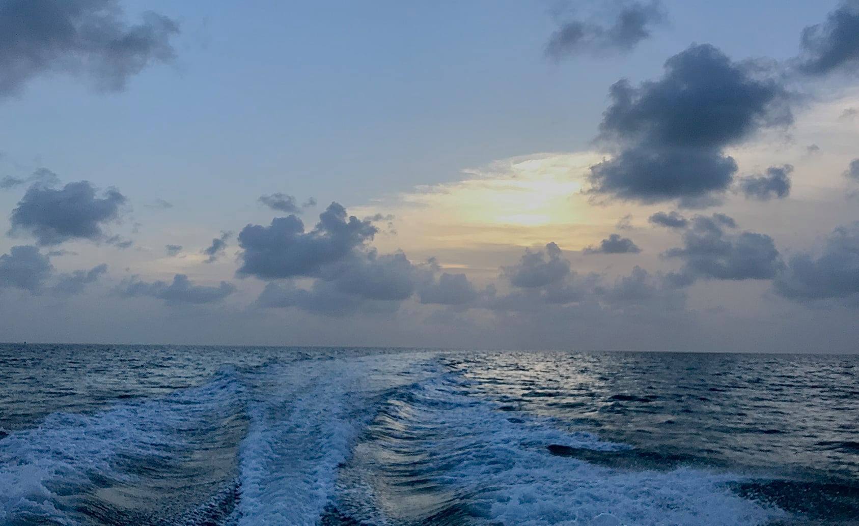 Boat wake trailing across ocean at sunrise