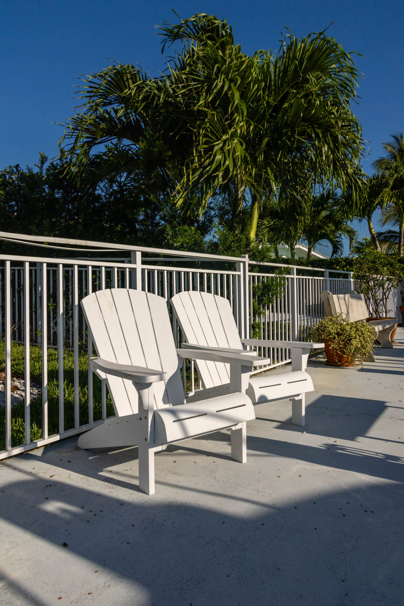 Two white Adirondack chairs on sunny patio