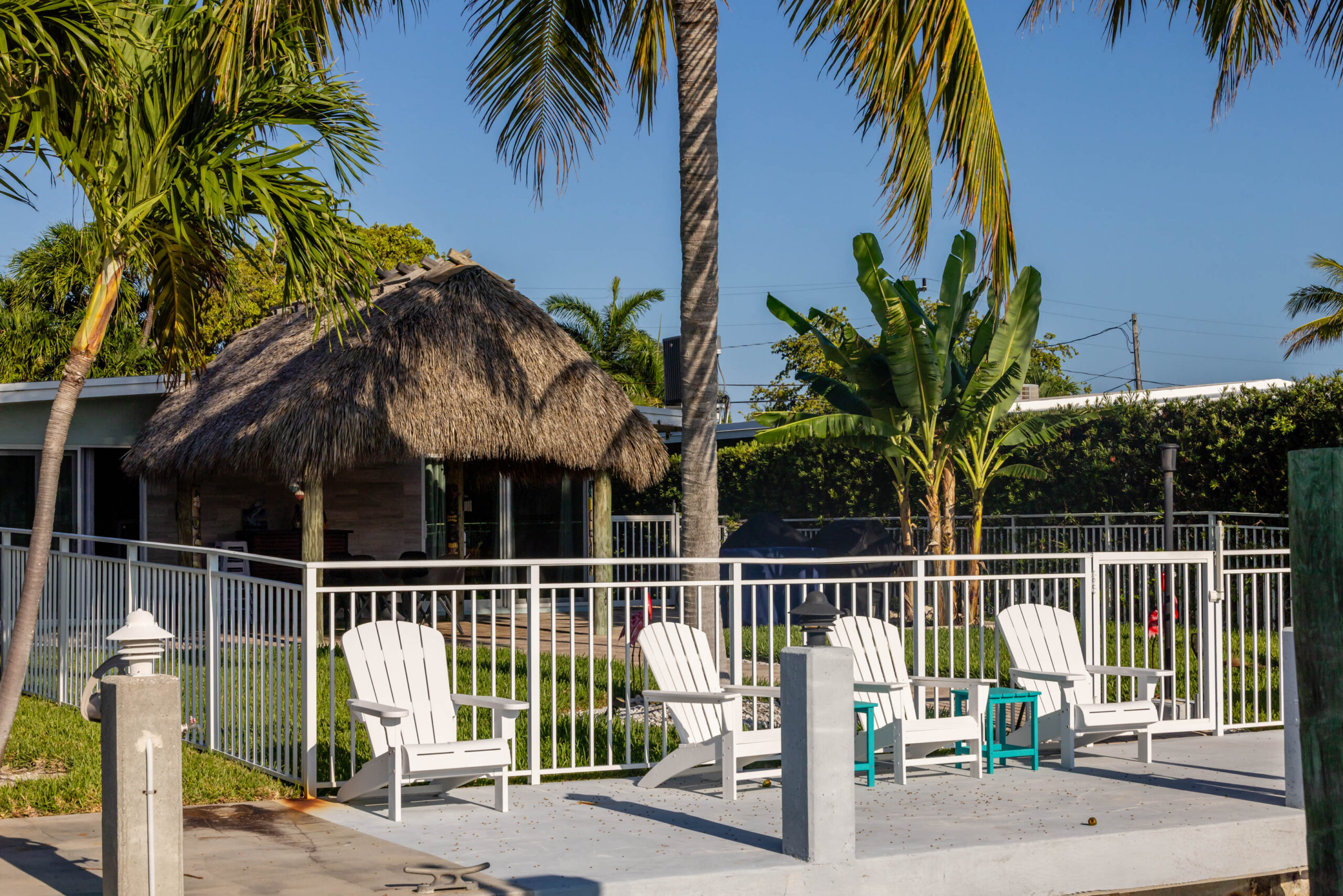 Waterfront dock with white Adirondack chairs, tiki hut