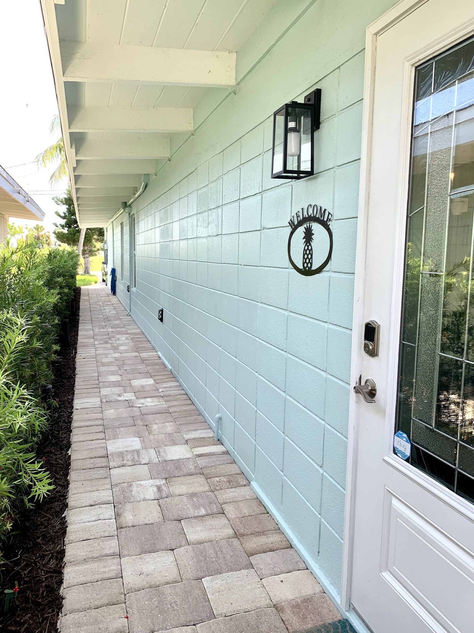 Paved walkway along light blue house with pineapple